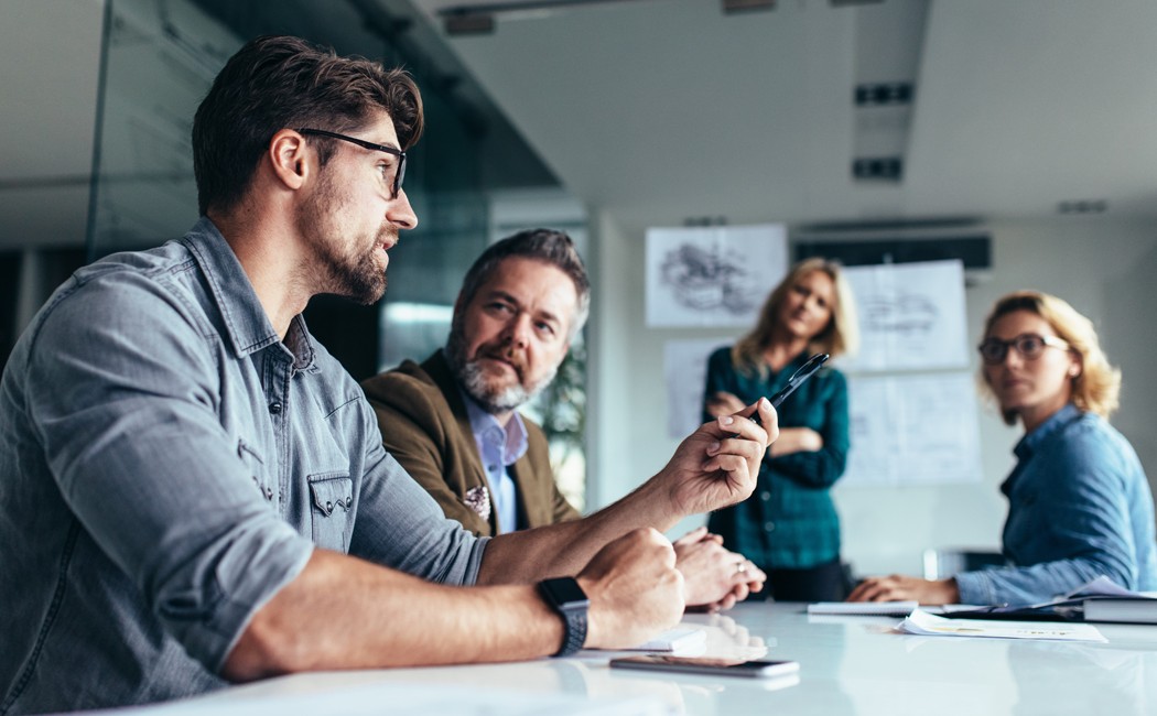 Four employees meeting in conference room - VMware licensing changes and the road ahead | DXC Technology Insights