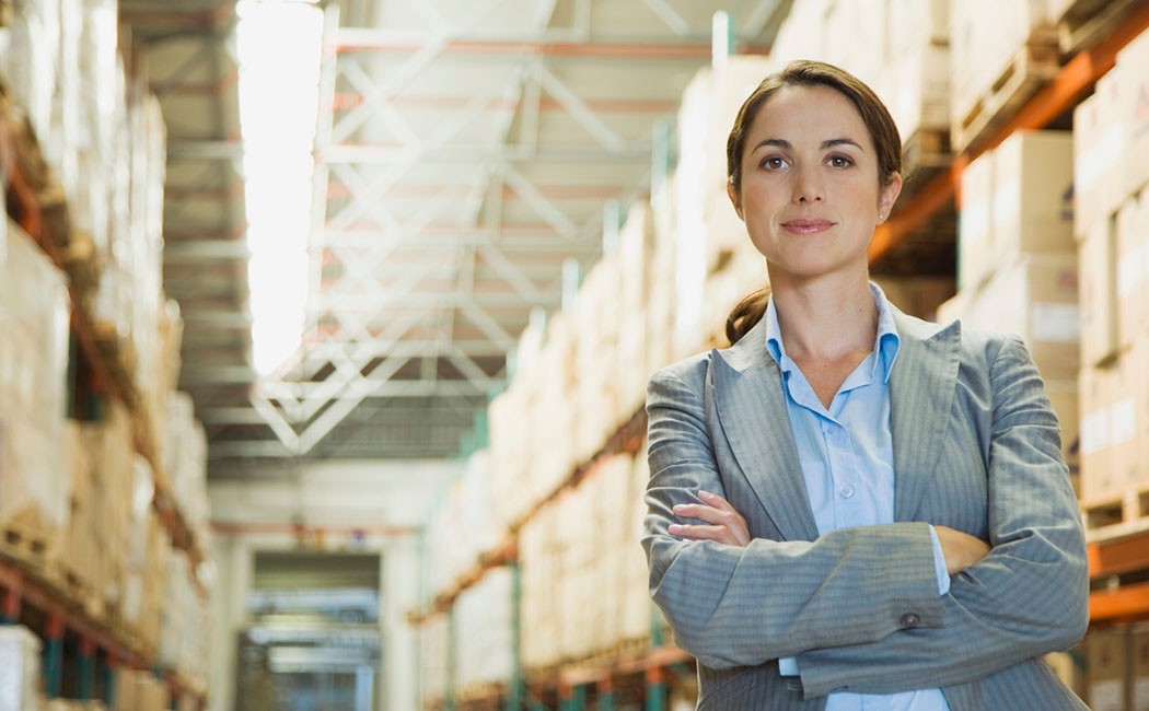 Female executive in blue shirt and jacket standing next to shelves in warehouse, Enterprise Applications | DXC Technology