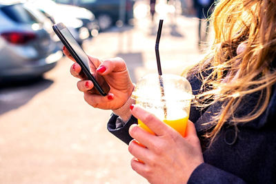 Woman outside on her smartphone with tea in hand.