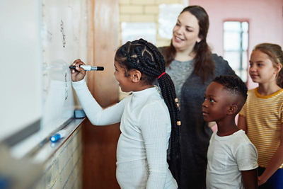 Teacher watching a student write on the whiteboard.