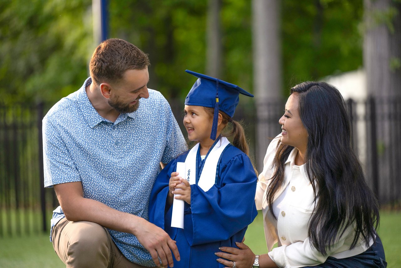 A young girl in a graduation cap and gown with her smiling parents.