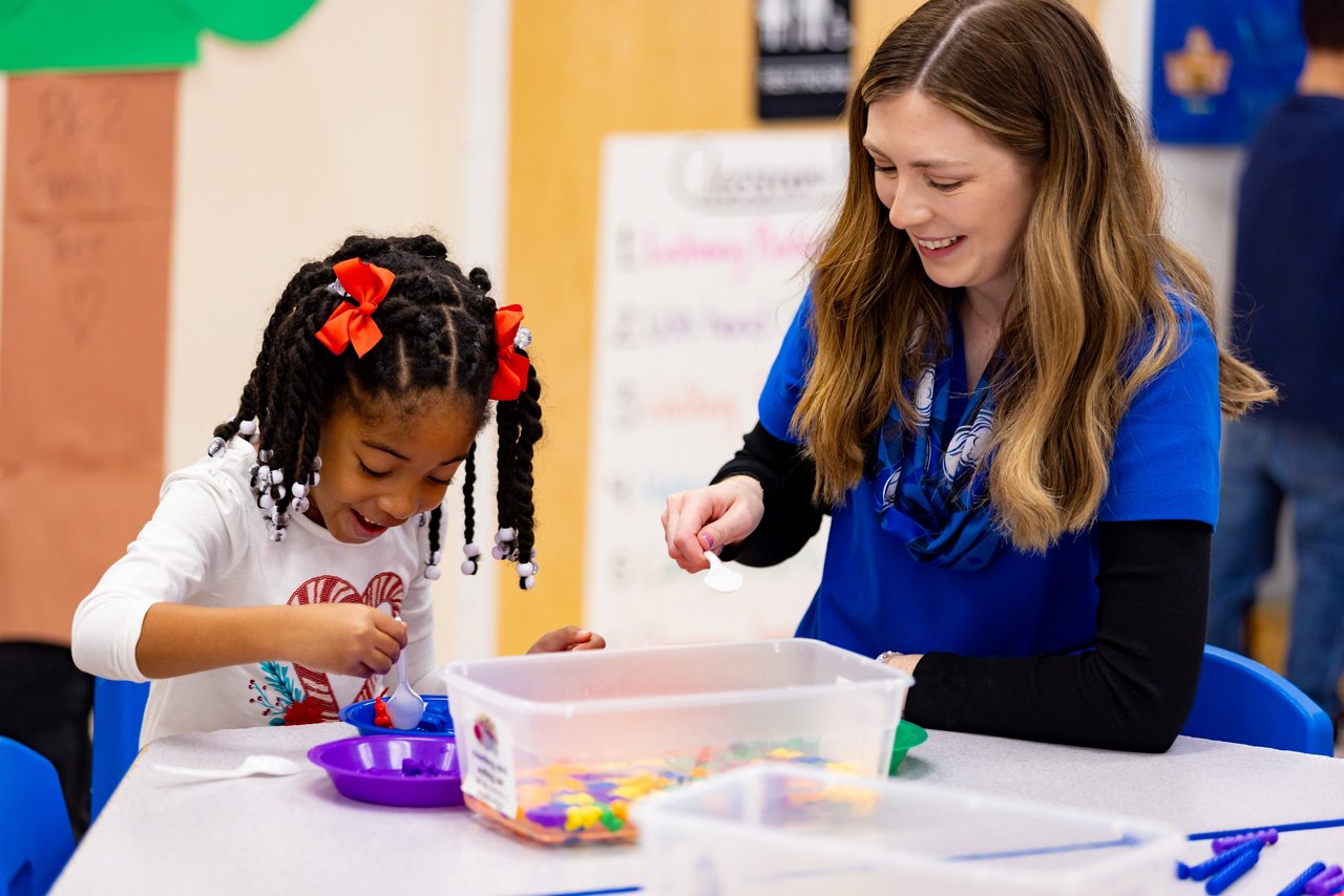 A teacher and child working on a project at a table in a preschool classroom