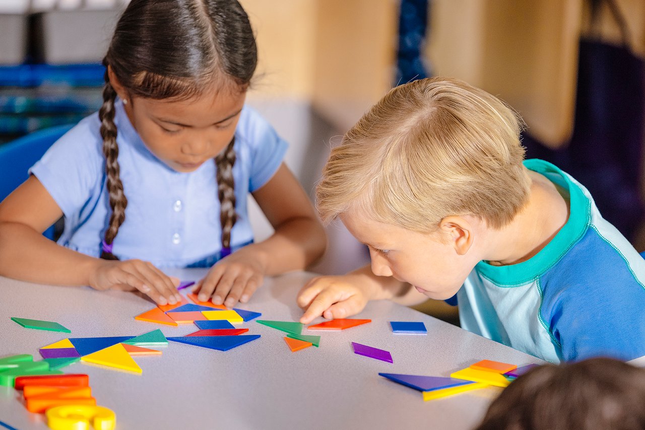 Children creating tangrams at a table in a preschool classroom