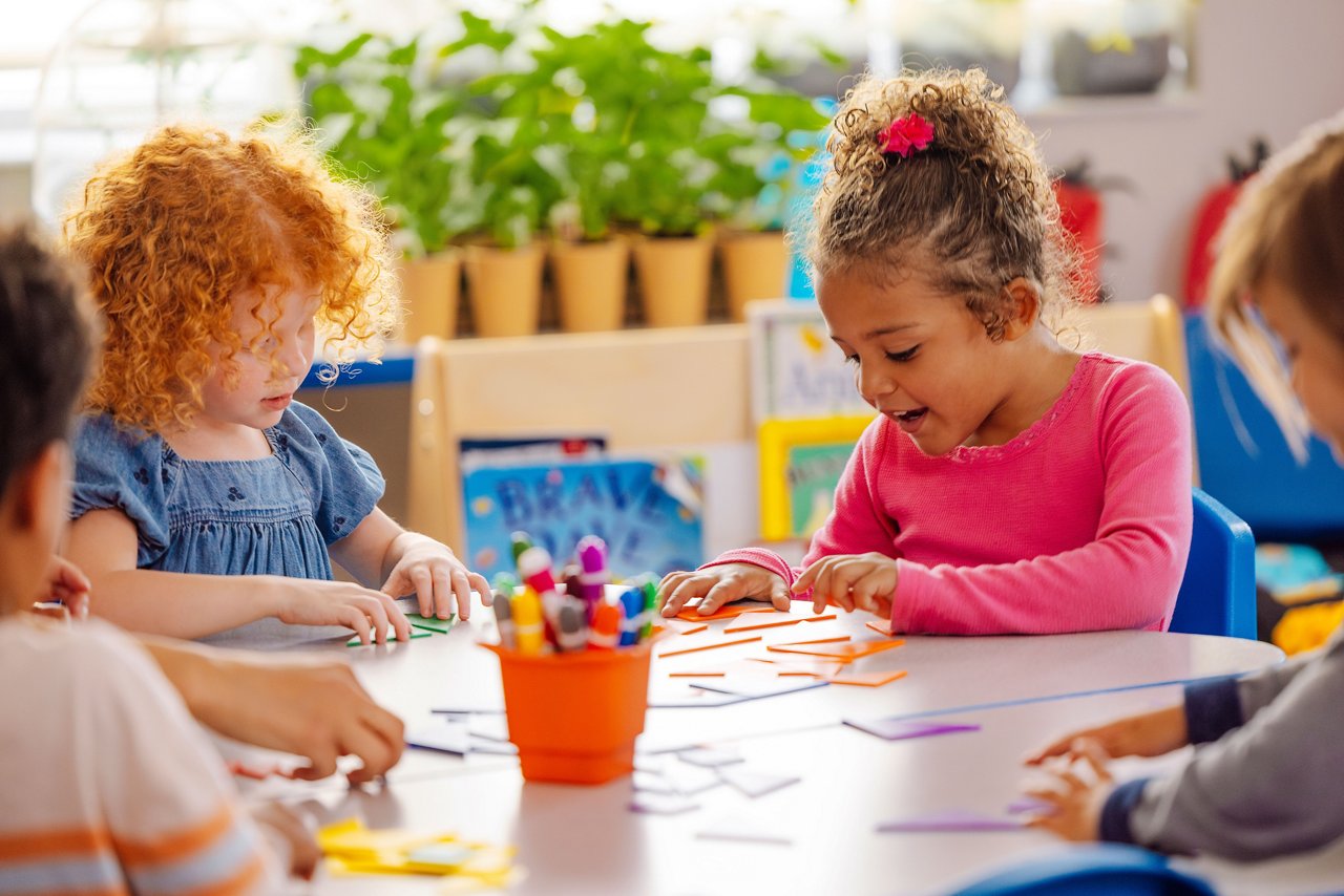 Children sitting at a table in a preschool classroom working on tangrams