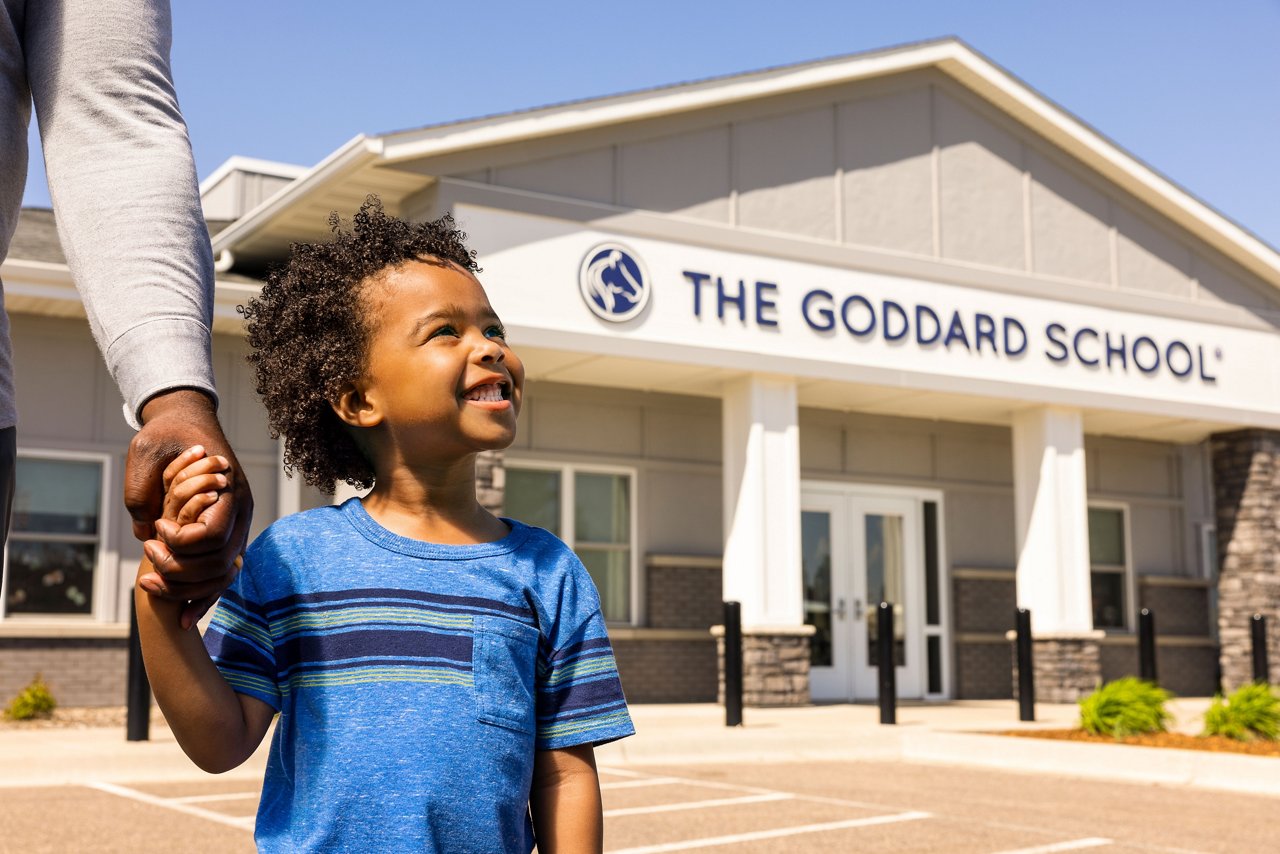 Smiling child holding his dad's hand outside of a Goddard School
