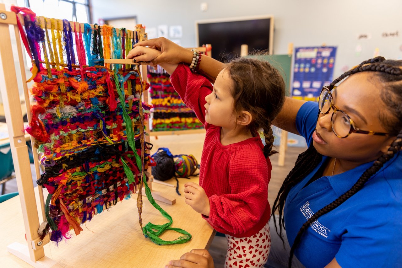Young child examining a display of colorful yarn with teacher