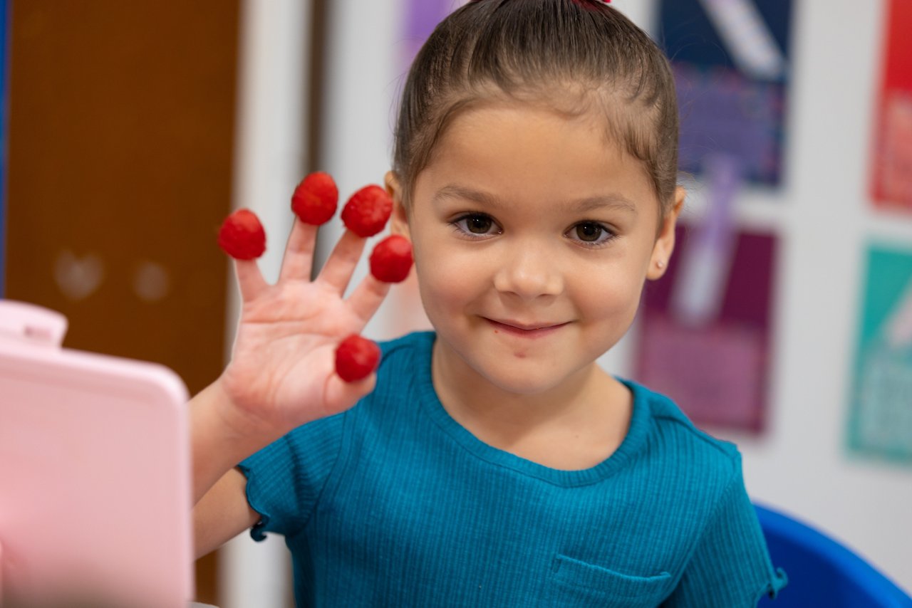 A young girl with raspberries on her fingertips smiling for the camera
