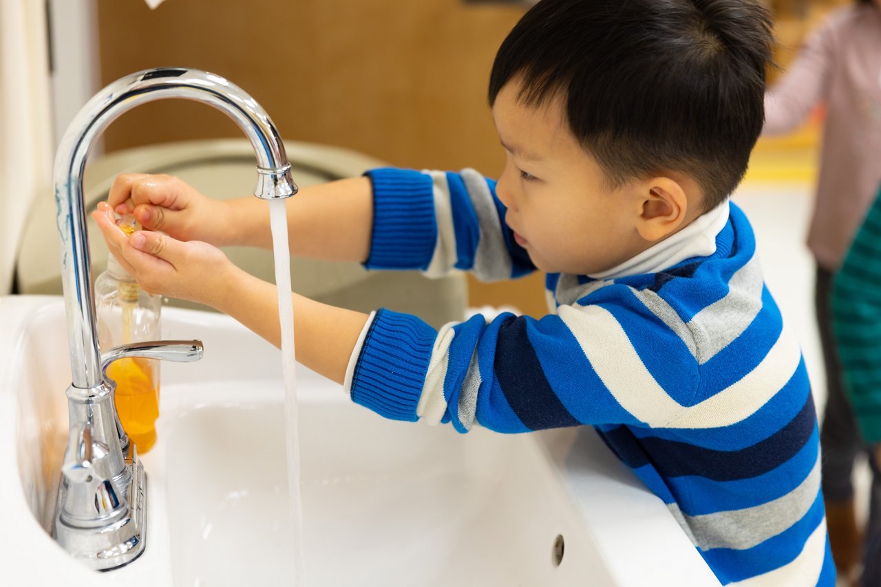 child at sink washing hands with soap