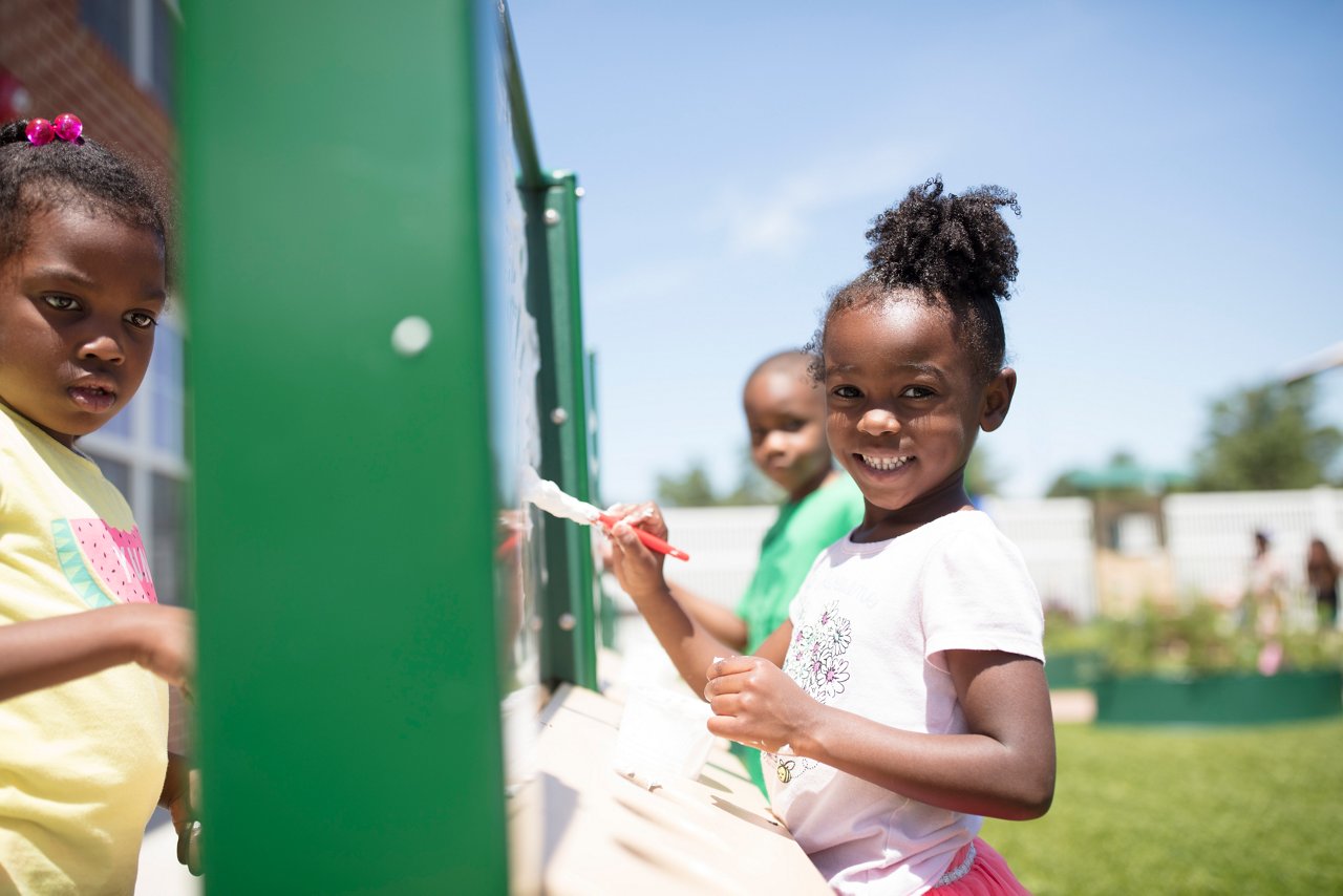 African American children playing and painting at outdoor classroom board