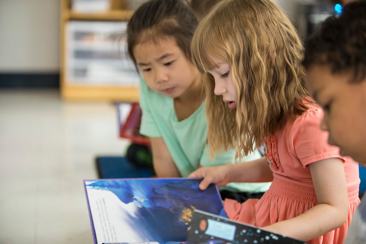 Three children sitting on floor looking at books