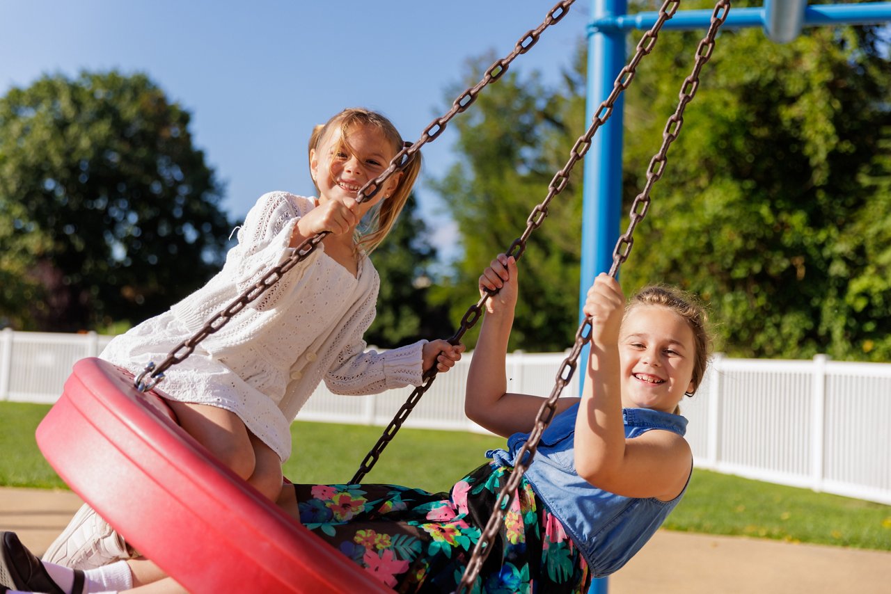 Two young girls playing on a tire swing on a preschool playground