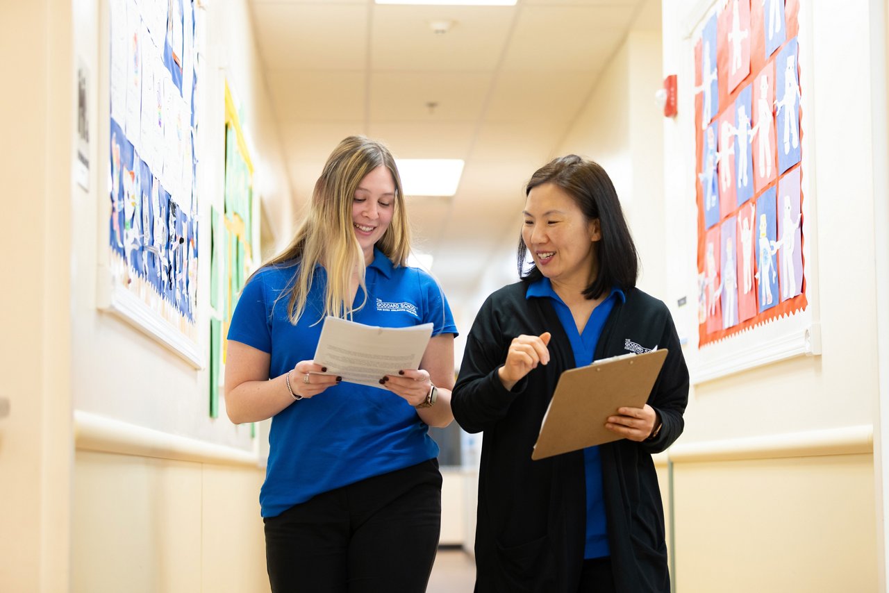 A franchisee and teacher walking down a Goddard School hallway looking at notes