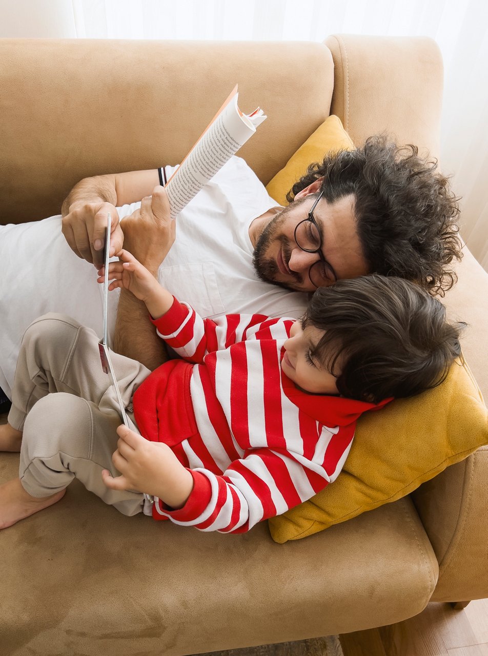 Father and son lying on sofa at home and reading book together