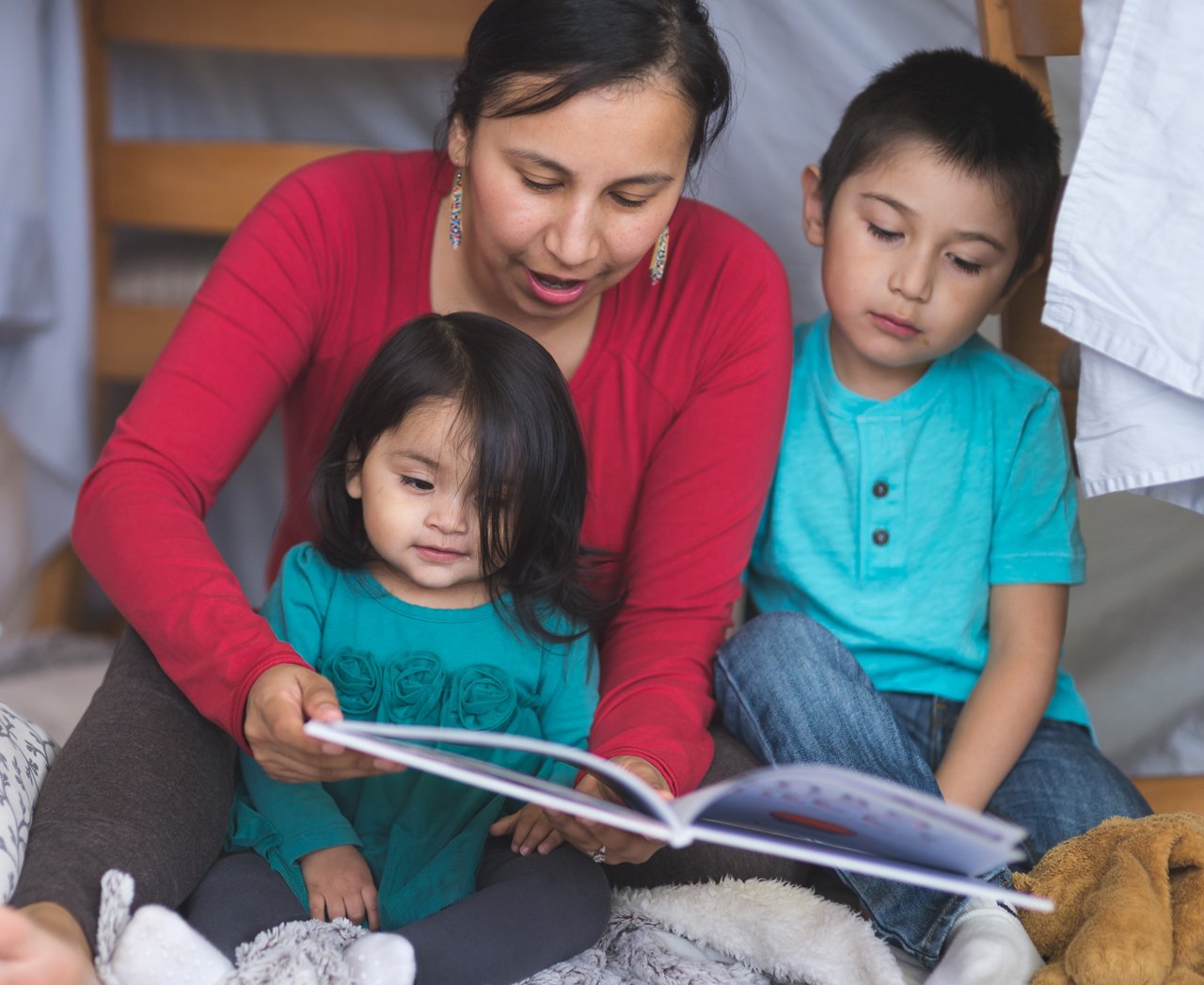Native American mom reads with her two children under makeshift fort in living room