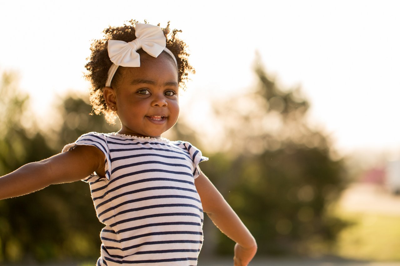 Smiling African American girl wearing bow with arms outstretched outdoors