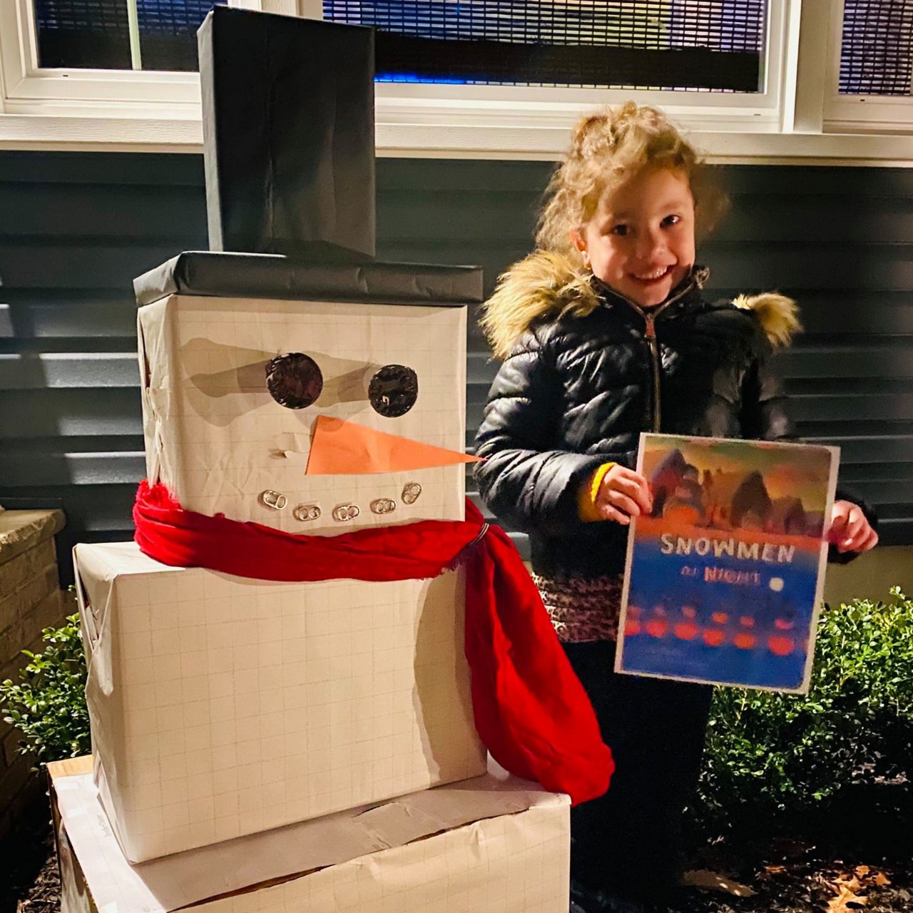 A young girls standing next to a snowman made out of cardboard boxes