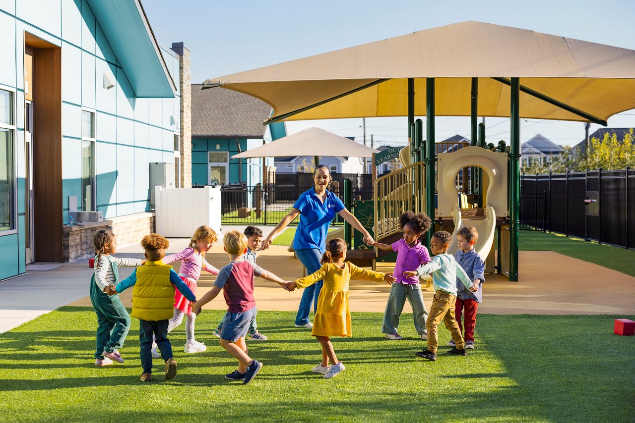 Children and teacher holding hands and walking in a circle together on a preschool playground.