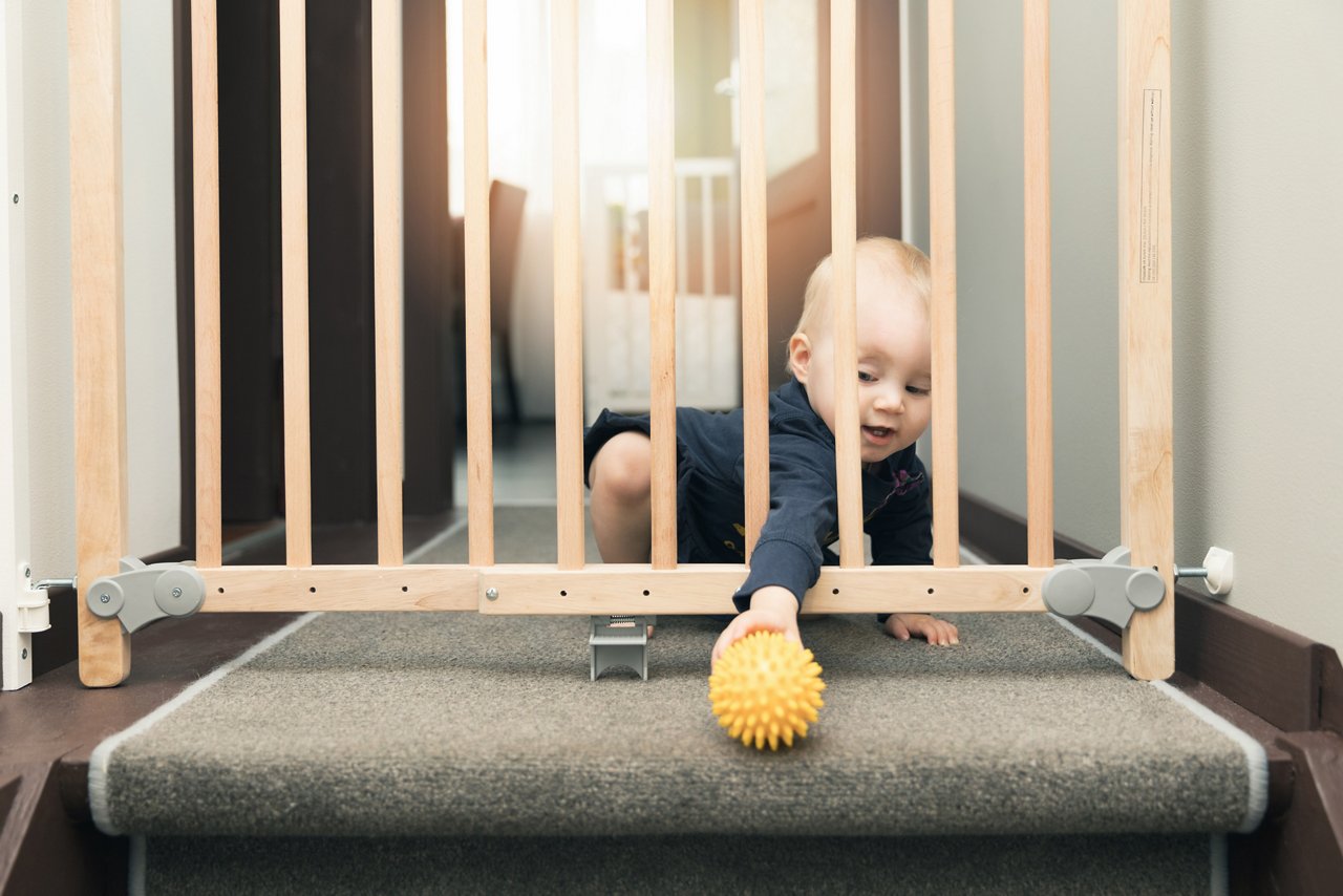baby reaching for ball through baby gate at top of stairs