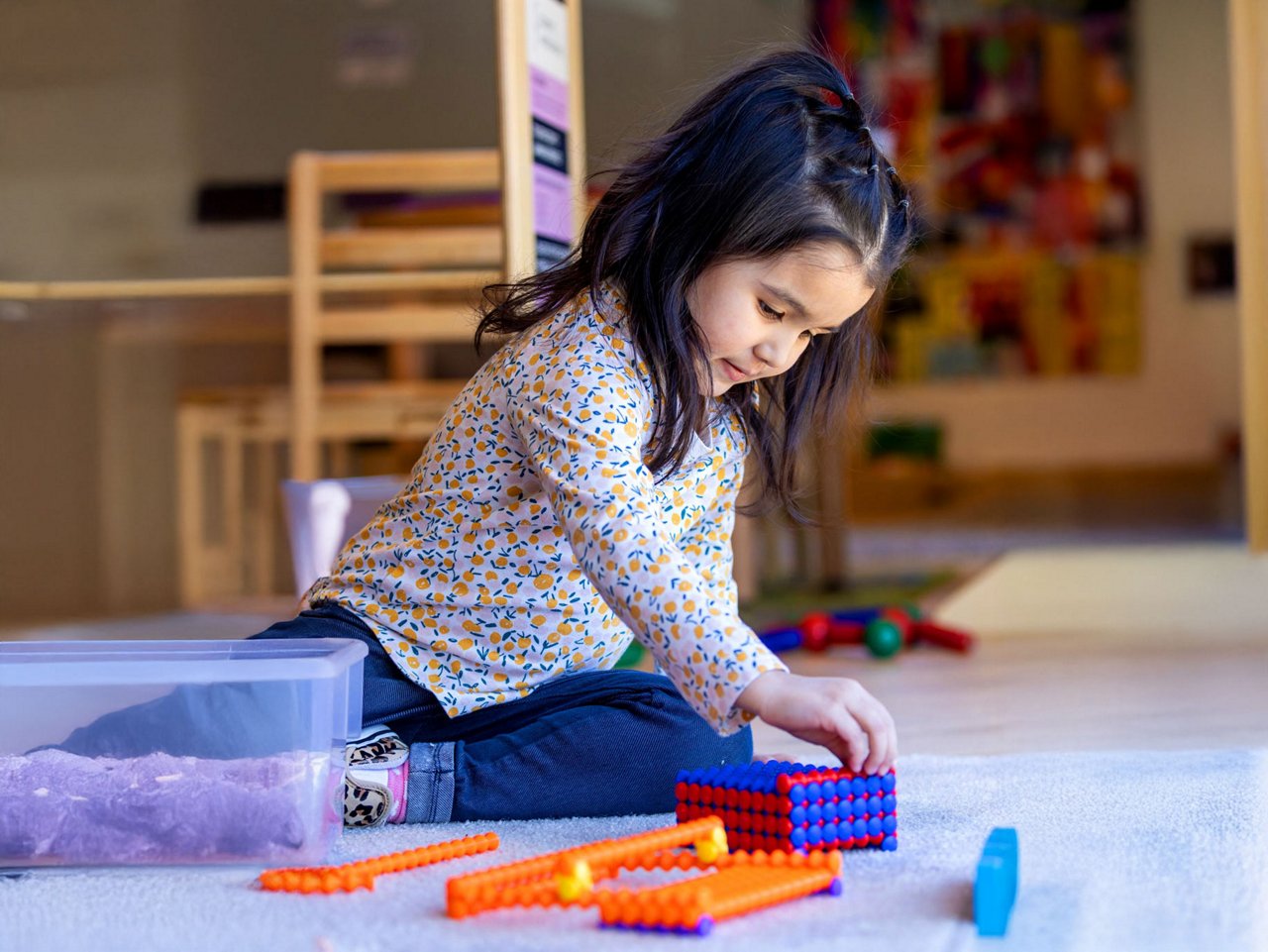 Preschool child engaging in creative play with colorful interlocking building blocks in a vibrant indoor classroom setting—supporting early learning and fine motor skill development.