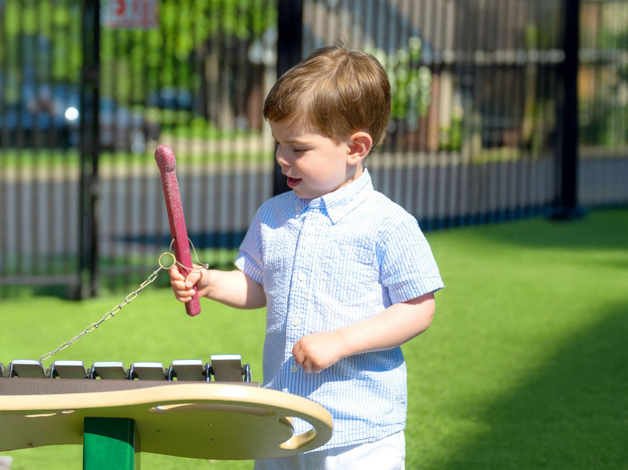 Preschool child exploring music outdoors with a colorful xylophone and mallet on a grassy play area—encouraging sensory development and creative expression in early childhood education.