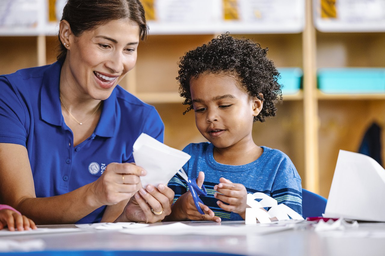Child and a Goddard preschool teacher making paper snowflakes