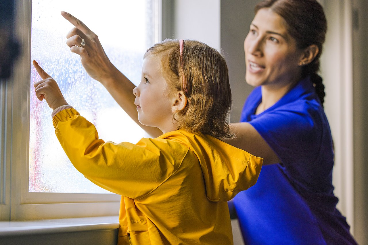 Child and Goddard preschool teacher touching a window with raindrops on the outside
