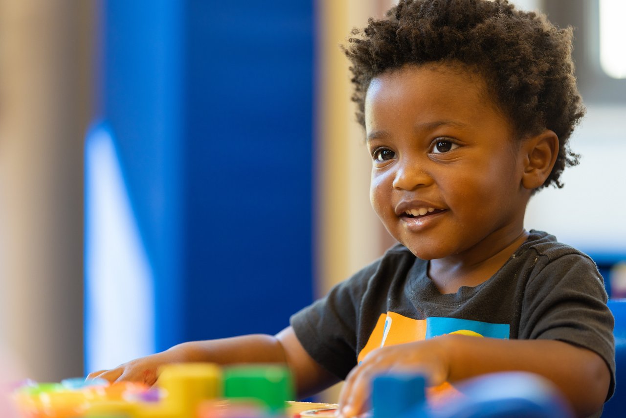 Young child playing with colorful toys at a preschool table, encouraging creativity, fine motor skills, and early childhood development in a vibrant learning space.