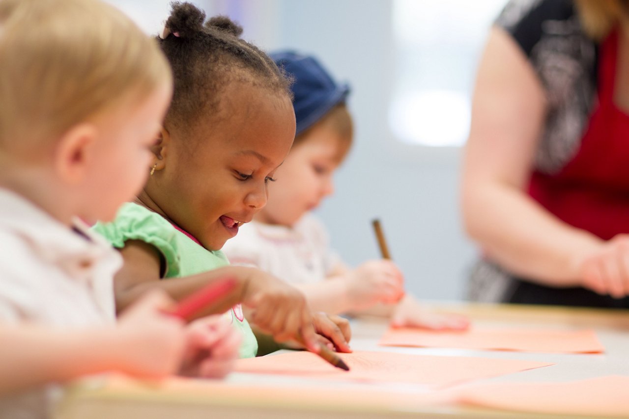 Preschool children coloring with crayons at a table in a classroom