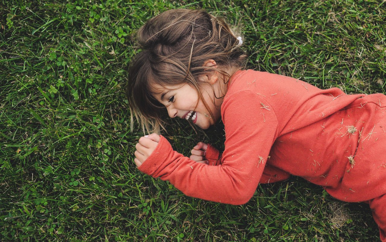 Cute little 4 year old girl laughing, joyful and full of happiness and smiles rolling in fresh spring grass, messy and fun, candid moment in childhood