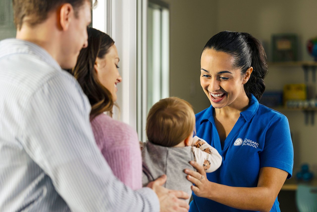 Goddard School teacher greeting parents with baby