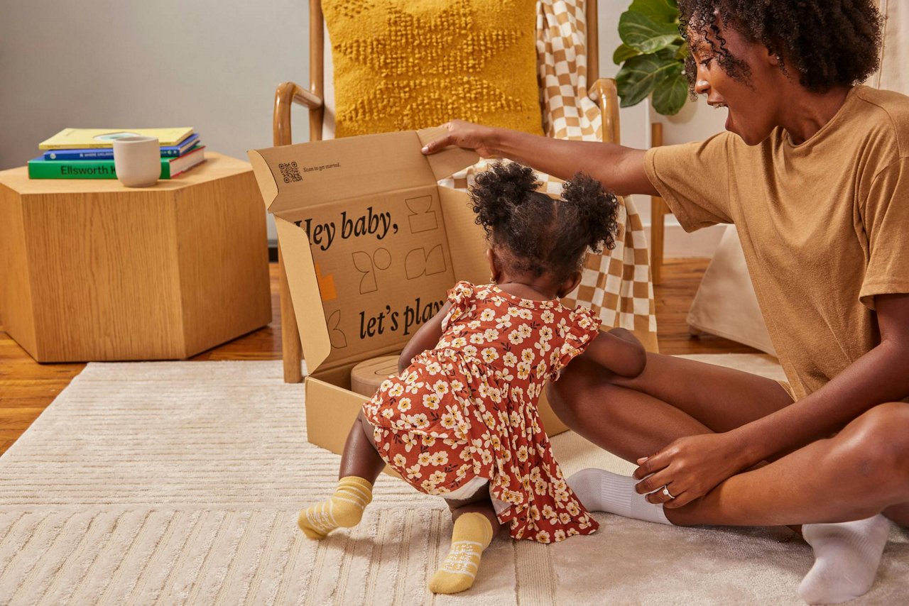 A mother and daughter sitting on the floor opening a delivery box