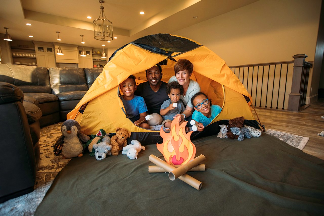 A father and mother, camp in their home with a tent pitched in the family room. They are using their imagination to experience the indoors.