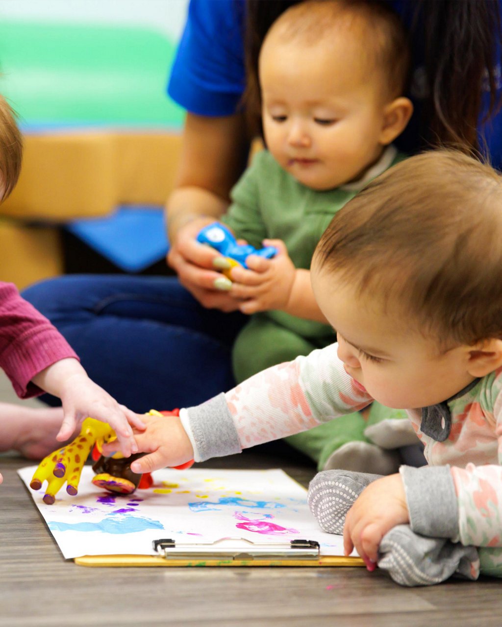 Infants playing using toy animals to stamp paint into an artistic picture