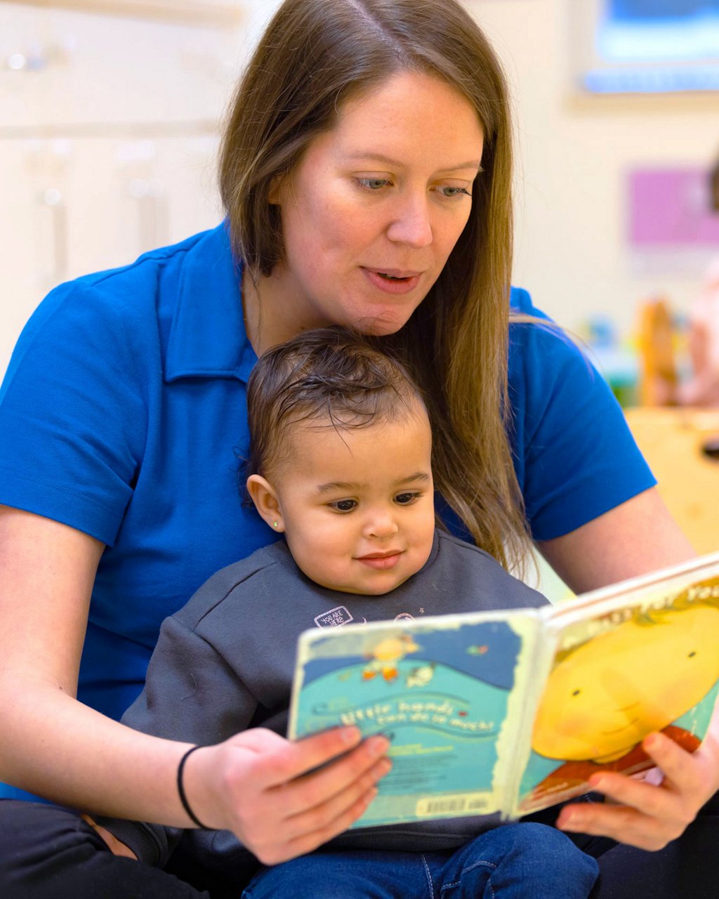 Infant sitting in a teacher's lap while being read a book