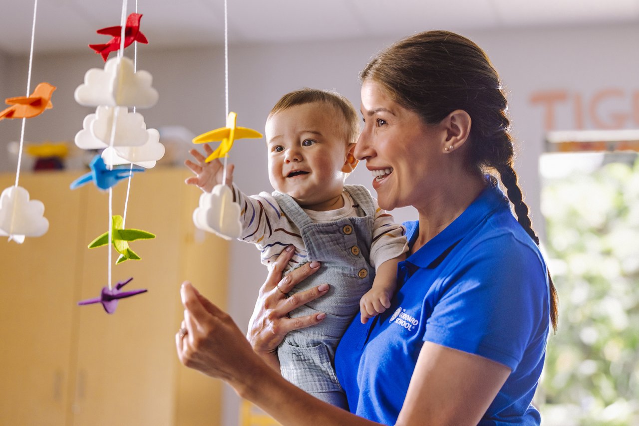 Teacher holding infant looking at a colorful bird mobile