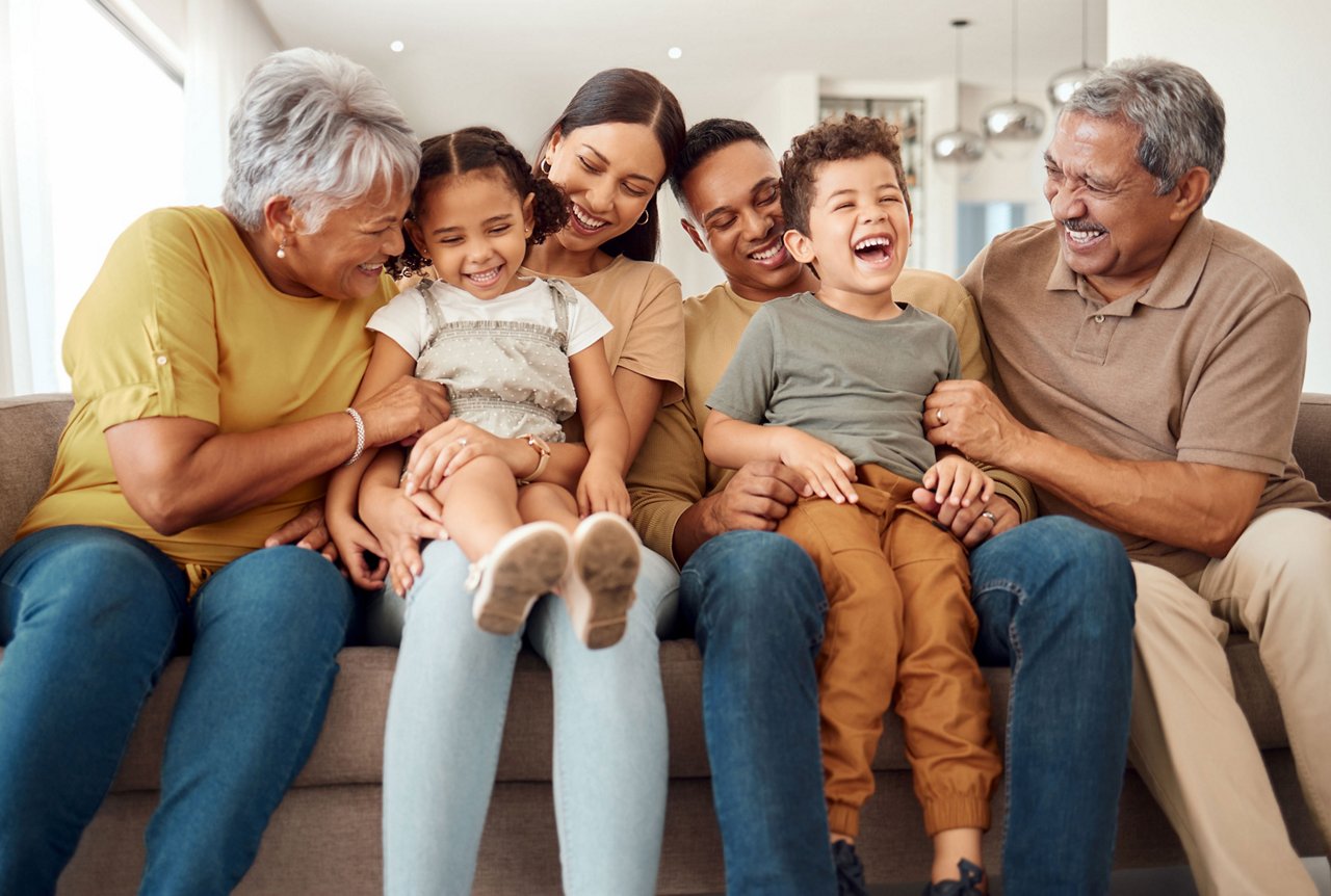 A family of grandparents, parents and children sitting on the couch laughing with each other