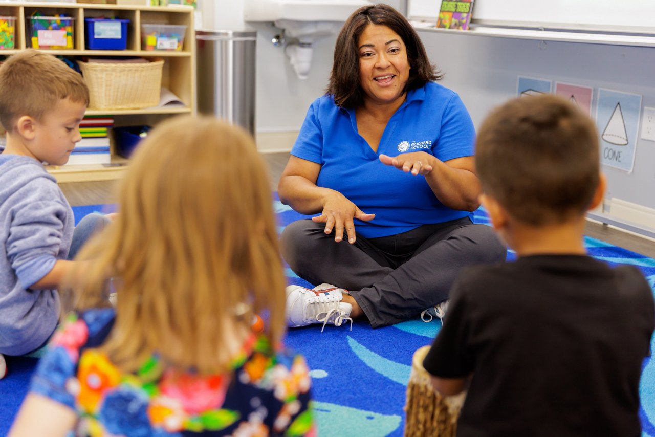 A teacher sitting on the floor with students playing a learning game