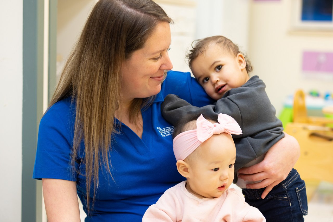 Teacher smiling at and holding two infants