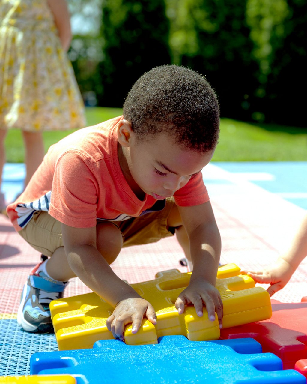 A child putting together a large outdoor puzzle 