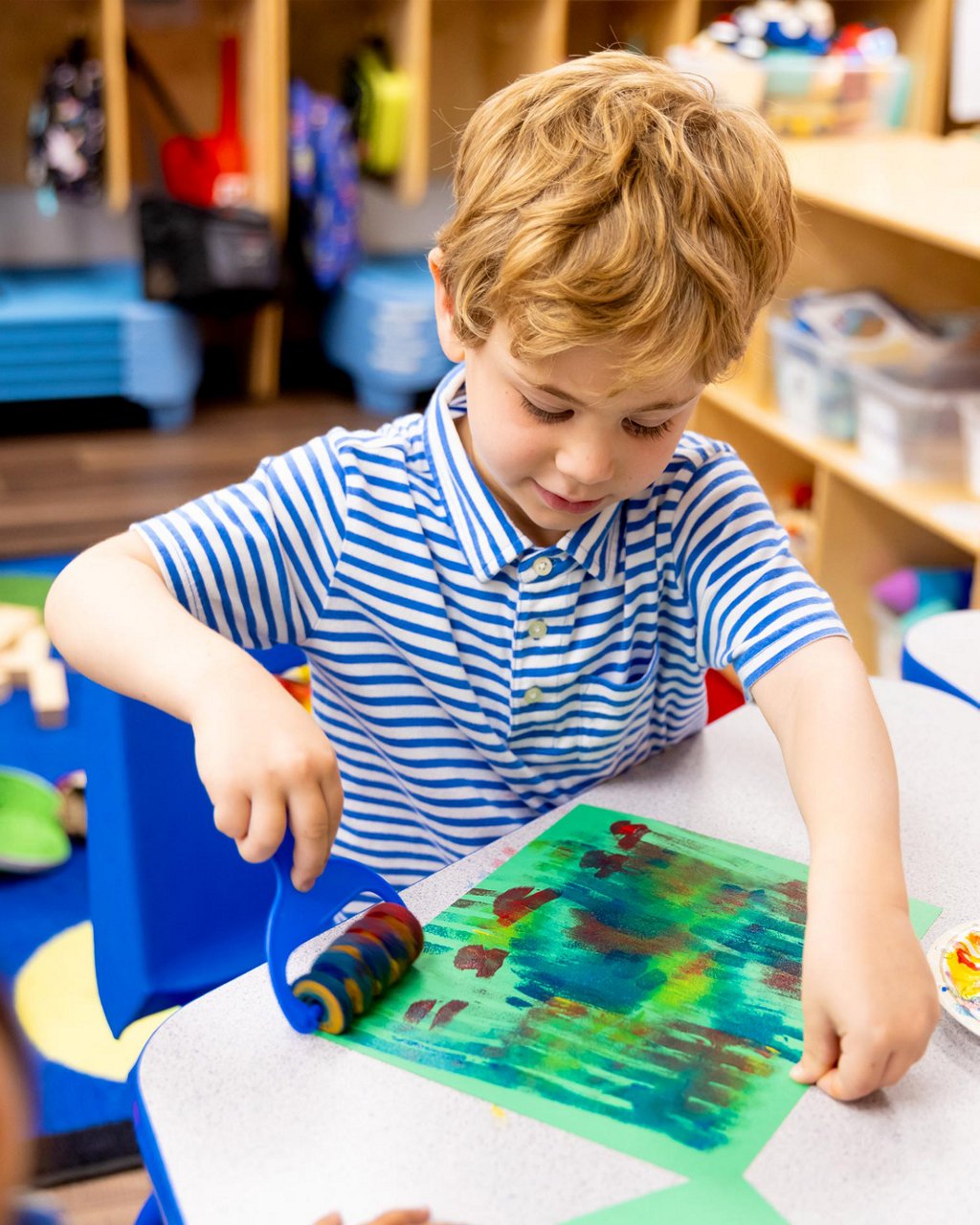 A child using a roller to paint on construction paper 