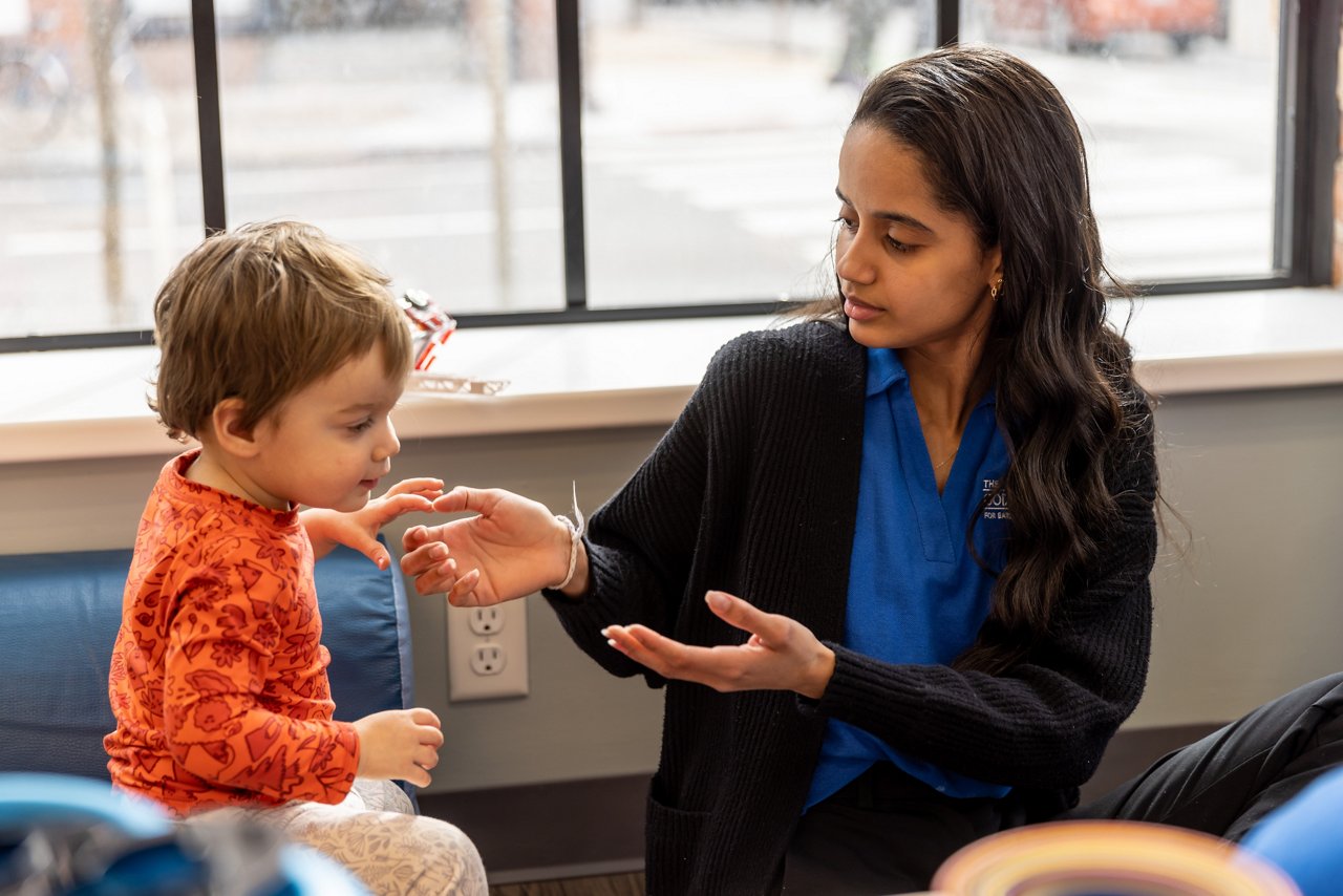 Preschool child interacting with a teacher in a sunlit classroom with large windows—supporting communication, connection, and individualized attention in early childhood education.
