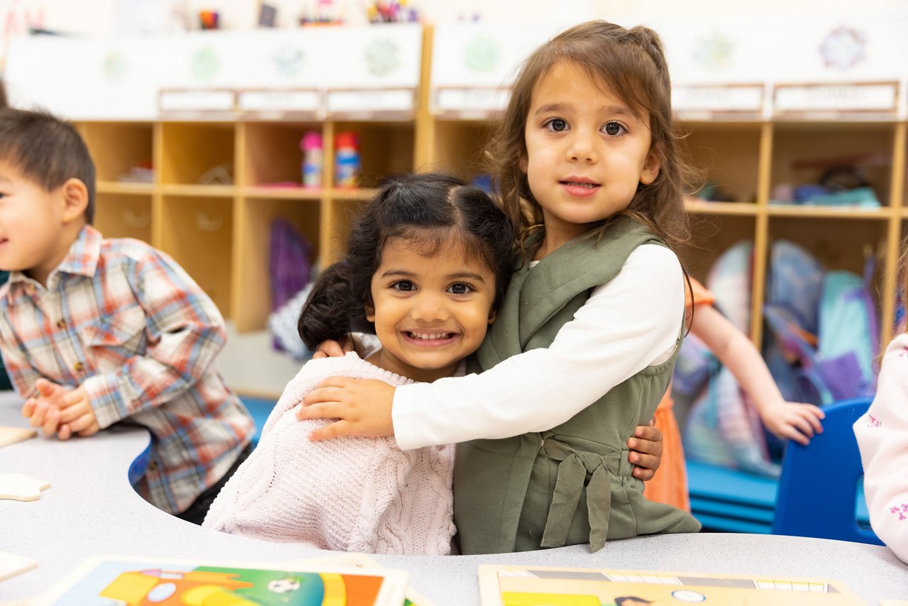 Preschool children gathered around a classroom table with books and learning materials, encouraging early literacy and collaborative learning in a nurturing environment.