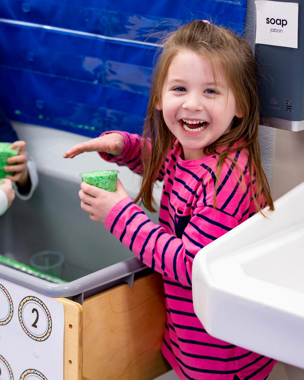 A smiling child holding a cup of green foam 