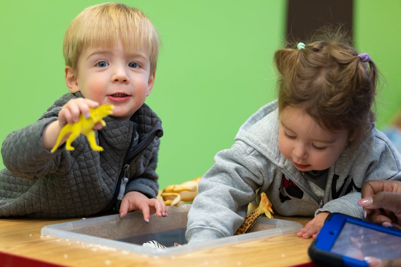 Preschoolers engaging in hands-on play with toys at a classroom table, supporting early learning through sensory exploration and social interaction.
