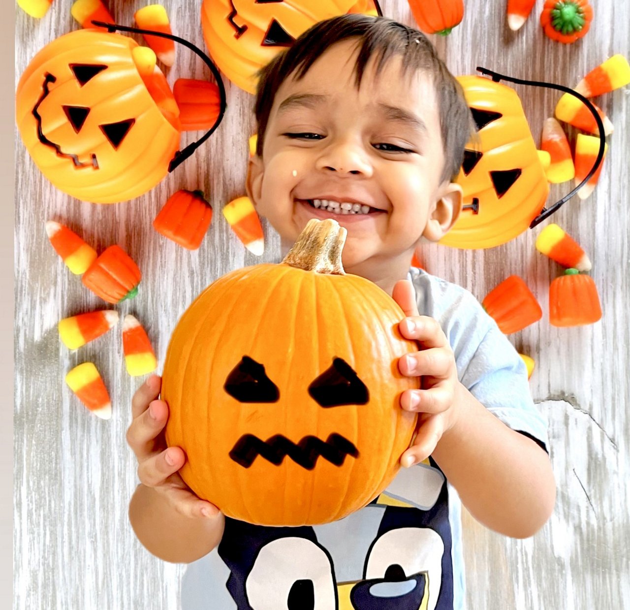 Little boy smiling holding a small painted jack-o-lantern with a background of Halloween treats