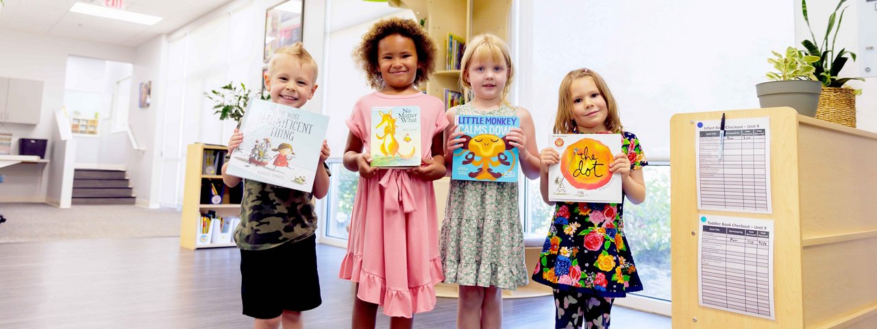 Four children smiling holding up books in a library