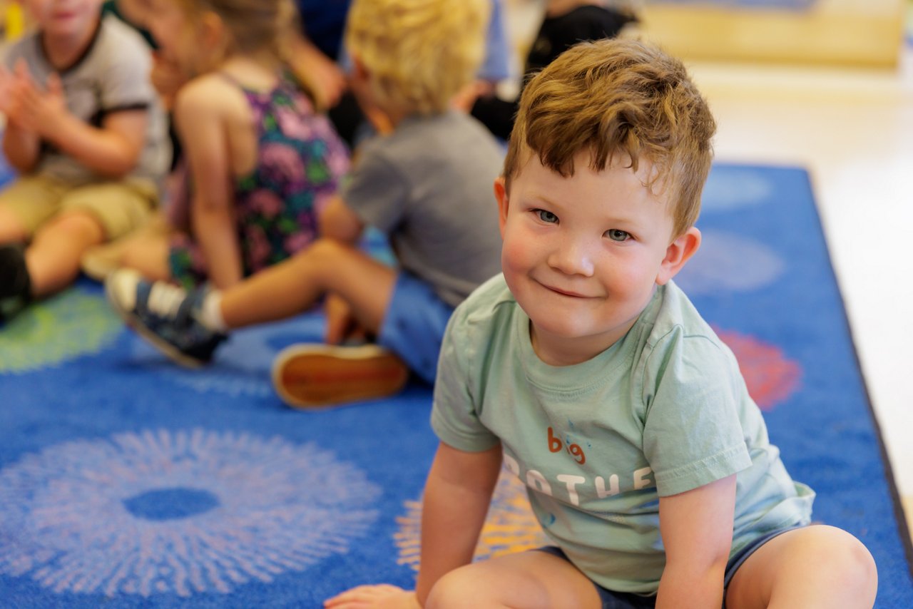 Group of preschool children sitting on a colorful classroom carpet, participating in early learning activities that promote social skills and classroom engagement.