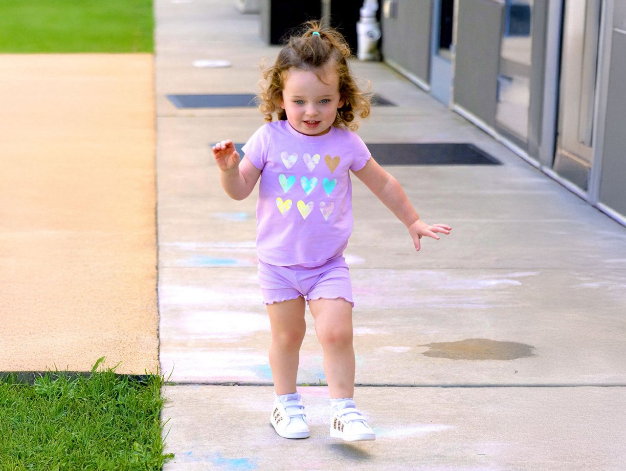 Preschool child walking along a sidewalk with colorful chalk drawings, promoting outdoor exploration and creative expression in a safe early learning environment.