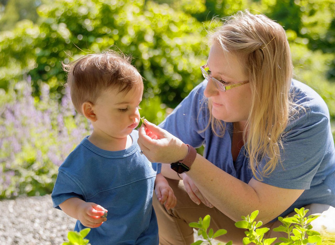 Preschool child exploring nature with a teacher in a garden setting — hands-on learning experience promoting curiosity, sensory development, and environmental awareness.