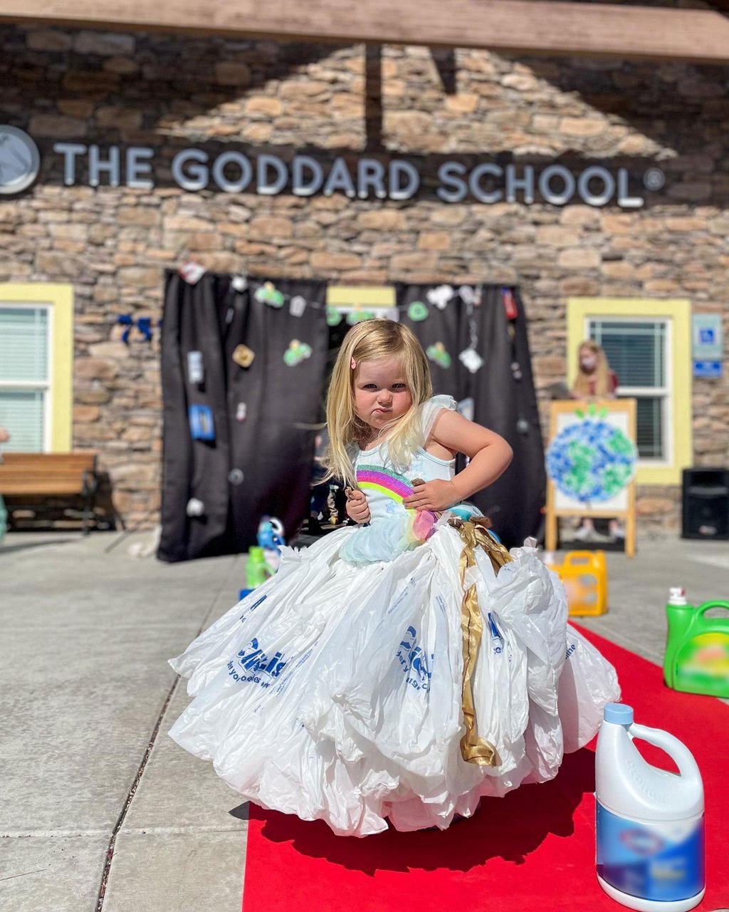 Little girl standing on a red carpet in front of a Goddard School in an upcycled dress
